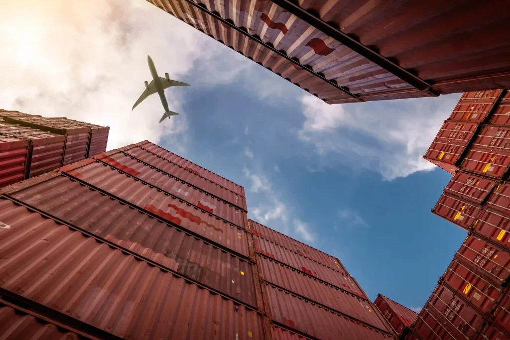 Cargo plane flying over cargo crates that are stacked on top of one another