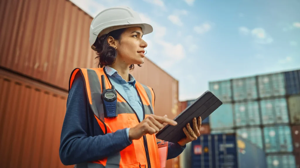 Smiling portrait of industrial worker in white hard hat and high-visibility vest working on a tablet computer